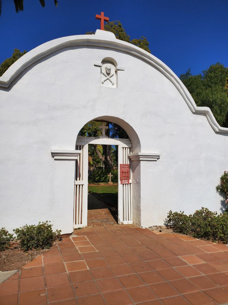 Photo showing the main entrance gate to the graveyard at Mission San Luis Rey in Oceanside, California.  The skull and crossbones design is visible above the gate.