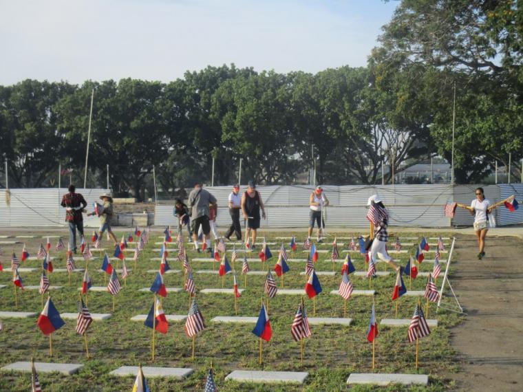 Photo for my international cemetery trivia quiz, from the American Battle Monuments Commission, showing volunteers placing U.S. and Philippine flags at graves at Clark Veterans Cemetery